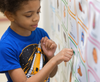 A young boy points to ‘go’ on a vinyl core vocabulary word sign featuring picture communication symbols